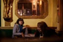 A woman in a pub looking over at 2 other women who are looking at a smartphone